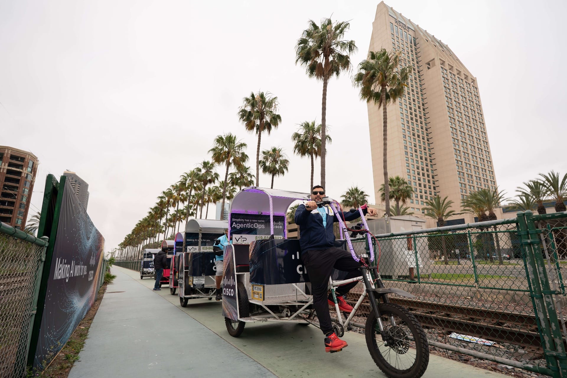 Cisco pedicab fleet with riders near Convention Center palm trees San Diego